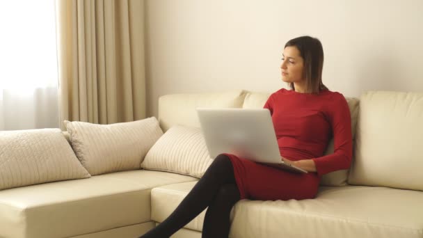 Schöne Frau mit kurzen Haaren sitzt auf dem Sofa im Zimmer und lächelt mit dem Laptop — Stockvideo