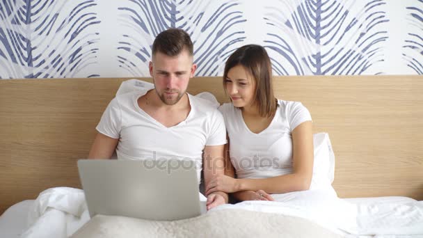 Νεαρό ζευγάρι με φορητό υπολογιστή, παρακολουθώντας την ταινία στο κρεβάτι — Αρχείο Βίντεο