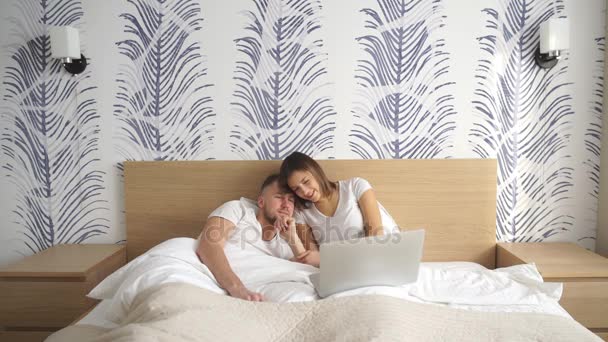 Smiling couple using a laptop lying on their bed — Stock Video