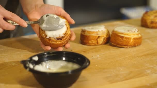 Womans Hand Spreading Frosting Across Freshly Baked Cinnamon Rolls — Stok Video