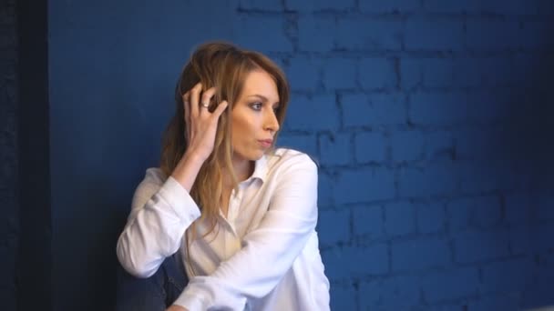 Mooie vrouw poseren voor de camera tegen een muur van de blauwe baksteen — Stockvideo