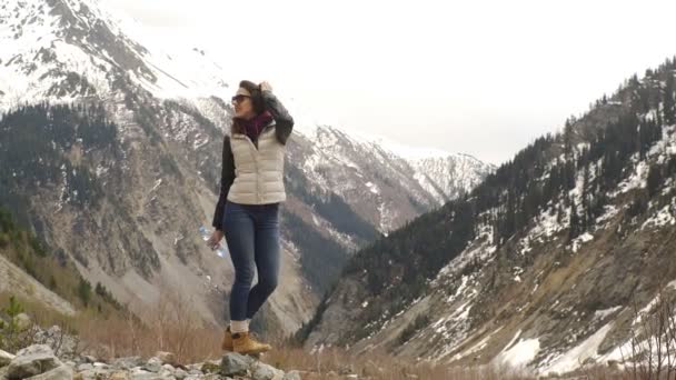 Beautiful woman traveler drinks water on a background of beautiful mountains — Stock Video