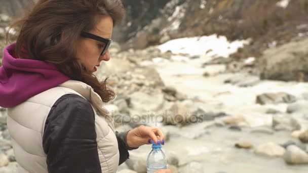 Молода жінка п'є воду на фоні гір — стокове відео