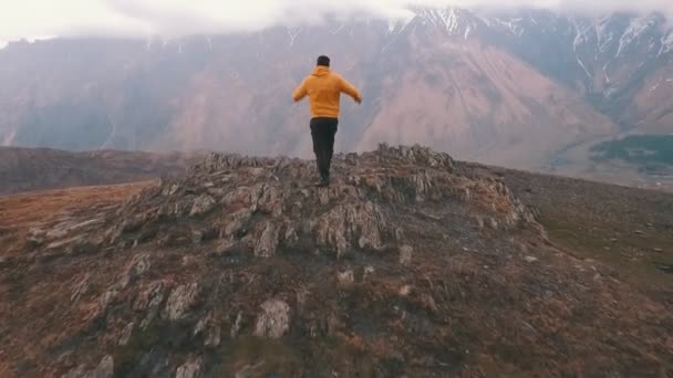 Um jovem levanta as mãos sobre um fundo de montanhas — Vídeo de Stock