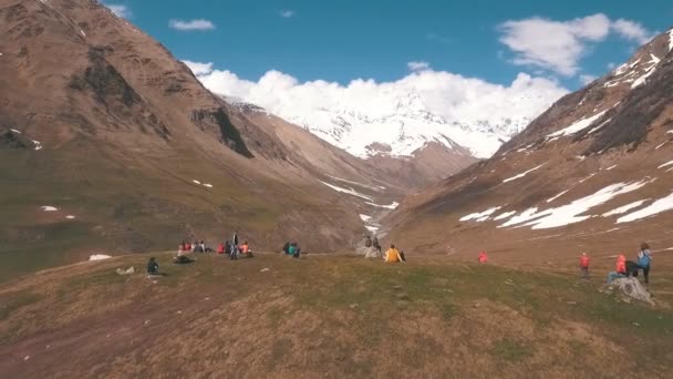 A group of tourists sits on a mountain and looking at the glacier — Stock Video