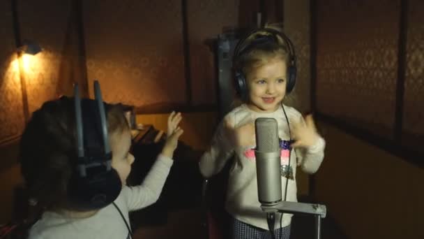 Zwei kleine Mädchen mit Kopfhörern singen in Mikrofon — Stockvideo