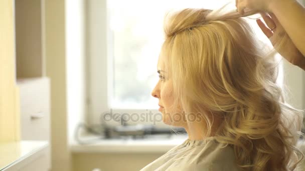 Il parrucchiere fa l'acconciatura di sera il primo piano su capelli biondi di donna d'affari in salone di bellezza — Video Stock