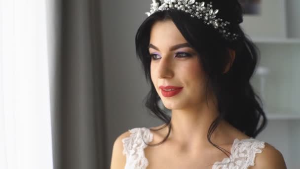 Невеста со свадебным букетом смотрит в окно и улыбается в камеру — стоковое видео