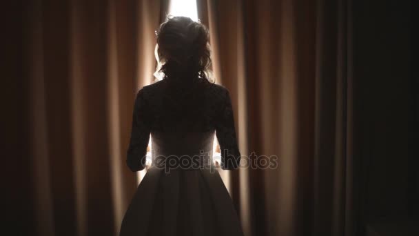 Mooie bruid opent de gordijnen in het donker — Stockvideo
