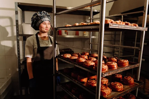 Bäcker steht neben Regalen mit frischen Brötchen — Stockfoto