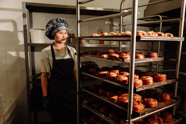Bäcker steht neben Regalen mit frischen Brötchen — Stockfoto