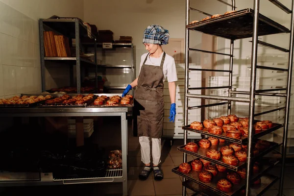 Baker se tient près des étagères avec des rouleaux frais — Photo