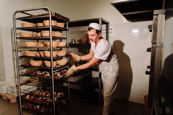 Schöne Bäckerin in Uniform mit einem Tablett voll frisch gebackenem Brot in der Manufaktur — Stockfoto