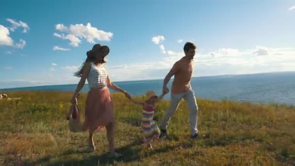 Красивая молодая семья бежит вдоль скалы на фоне реки и солнца — стоковое видео