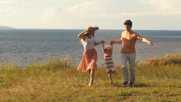 Schöne junge Familie läuft entlang der Klippe auf dem Hintergrund des Flusses und der Sonne — Stockvideo