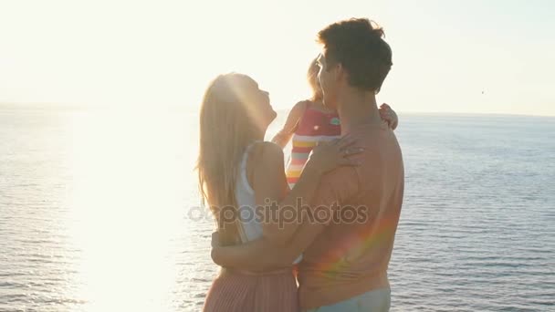 Счастливые родители, держащие дочь на руках и целующиеся — стоковое видео