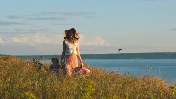 Красивая мать, идущая со своей маленькой дочерью в поле, вдоль скалы — стоковое видео
