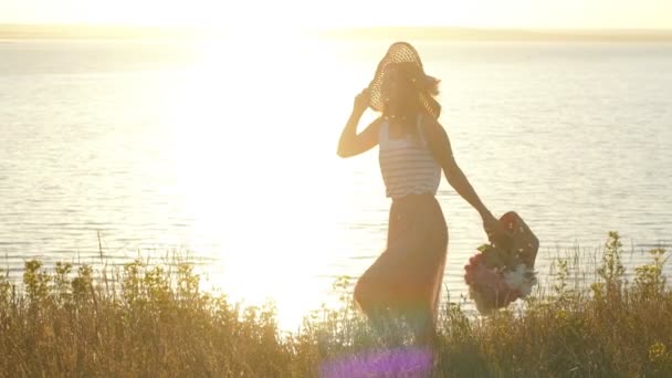 Красивая женщина в шляпе ходит по полю и волнам — стоковое видео
