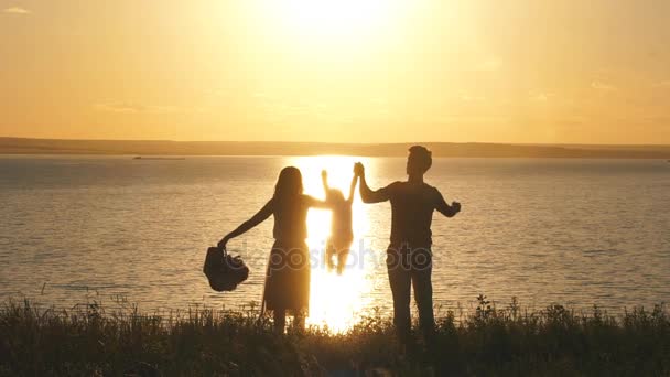 Glad mamma och pappa är på kanten av en klippa och höja händerna döttrar mot havet och solnedgång — Stockvideo