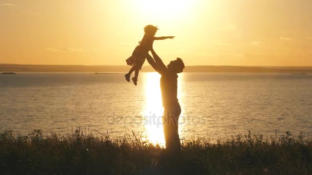 Батько кидає дитину в повітря на пляжі на заході сонця — стокове відео