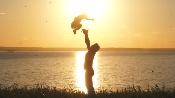 Vater wirft sein Kind bei Sonnenuntergang am Strand in die Luft — Stockvideo