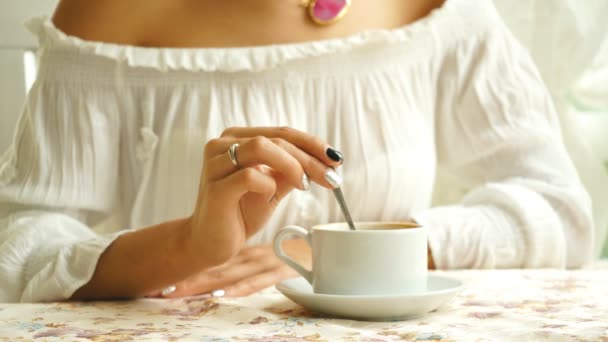 Красивая брюнетка в белой блузке, пьет кофе на яркой террасе — стоковое видео
