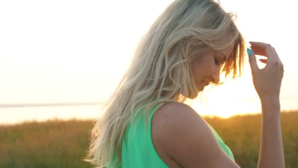 Hermosa rubia caminando en un campo al atardecer, primer plano — Vídeo de stock