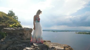 Sarışın kollarını yukarı bir uçurum, dikiz arka planda bir nehir kenarına yükseltir