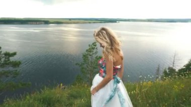 Sarışın kollarını yukarı bir uçurum, dikiz arka planda bir nehir kenarına yükseltir