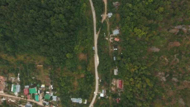 Вид с воздуха на деревню в лесу, горная дорога — стоковое видео