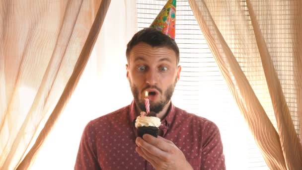 Mężczyzna w kapeluszu partii wydmuchuje świeca na cupcake — Wideo stockowe
