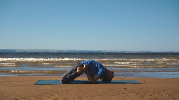 Fuerte hombre practicando difícil yoga pose en la playa — Vídeo de stock