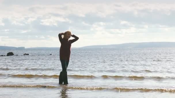 Ein junges Mädchen steht im Fluss und lächelt in Gummistiefeln — Stockvideo