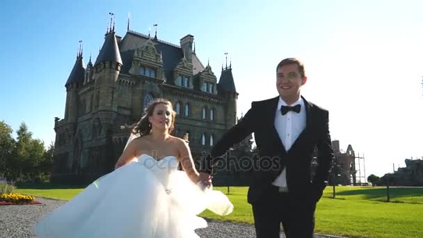 La novia y el novio corren cerca del viejo castillo — Vídeos de Stock