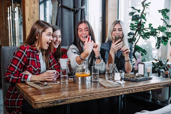 Quatre jeunes femmes assises dans un café en utilisant un téléphone intelligent et avoir une conversation drôle . — Photo