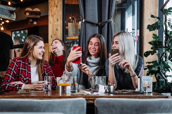 Quatro amigos olham para o telefone e riem — Fotografia de Stock