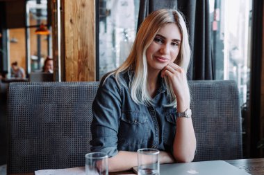 güzel bir sarışın bir kafe ve kamera gülümsüyor oturuyor