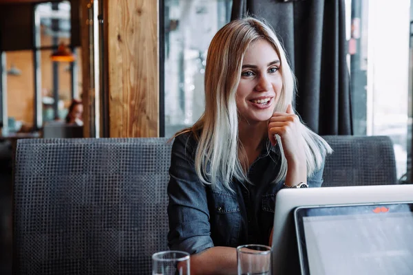 Güzel bir sarışın iş kadını bir kot gömlek bir restoranda oturur ve arkadaşları ile iletişim kurar — Stok fotoğraf