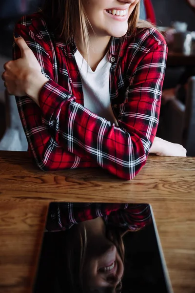 Молодая улыбающаяся деловая женщина, сидящая за столом в кафе. На столе планшетный компьютер и чашка кофе . — стоковое фото