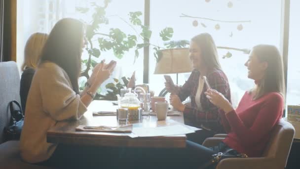 Ung kvinna delar något på hennes mobiltelefon med tre attraktiva skrattande flicka vänner — Stockvideo