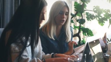 iki iş kadınları aktif bir kafede bir dizüstü bilgisayar üzerinde çalışan ve iş tartışıyor