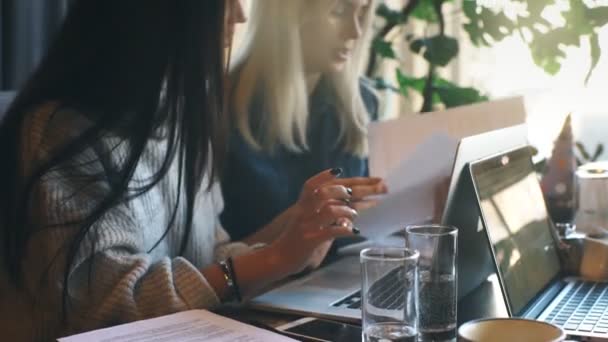 Deux femmes d'affaires travaillent activement sur un ordinateur portable dans un café et discutent du travail — Video