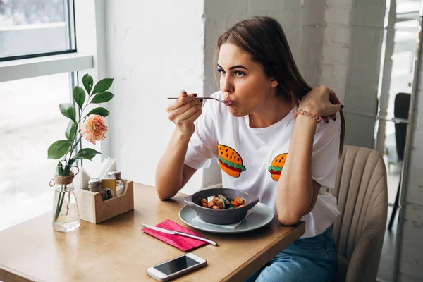 güzel bir genç kadın bir kafede yemek yiyen ve pencereden görünüyor