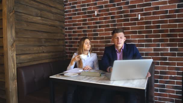 Dos jóvenes empresarios que trabajan en el ordenador portátil en la cafetería — Vídeos de Stock