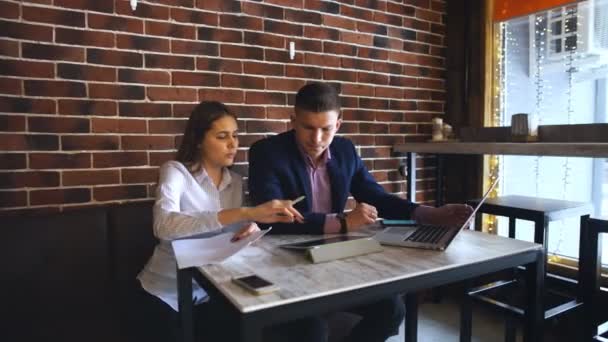 Dos jóvenes empresarios que trabajan en el ordenador portátil en la cafetería — Vídeos de Stock
