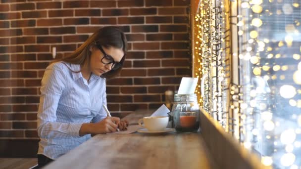 Een mooie jonge zakenvrouw werkt in een café en contracten tekenen — Stockvideo