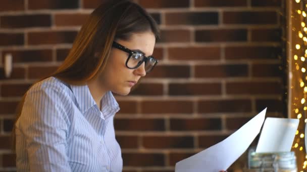 Kağıdın incelenmesi ve dizüstü bilgisayarda yazarak genç iş kadını — Stok video