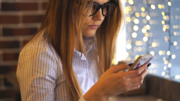 Mujer joven sentada en la cafetería en la mesa de madera y usando un teléfono inteligente . — Vídeos de Stock