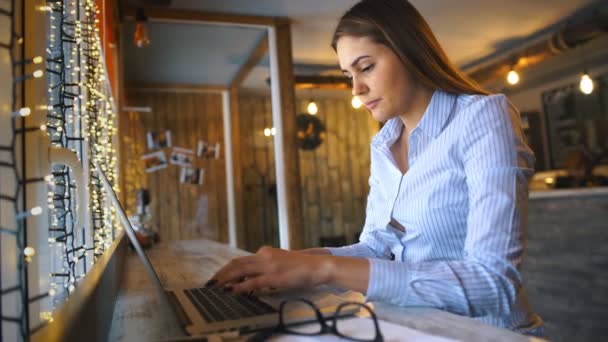 Vista lateral de hermosas mujeres jóvenes manos ocupadas trabajando en su computadora portátil sentado en la mesa de madera en una cafetería — Vídeos de Stock