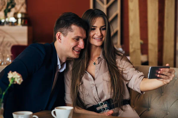 Радостная любящая пара, наслаждающаяся современными технологиями, развлекающаяся, запечатлевающая яркие моменты отпуска в кафе — стоковое фото